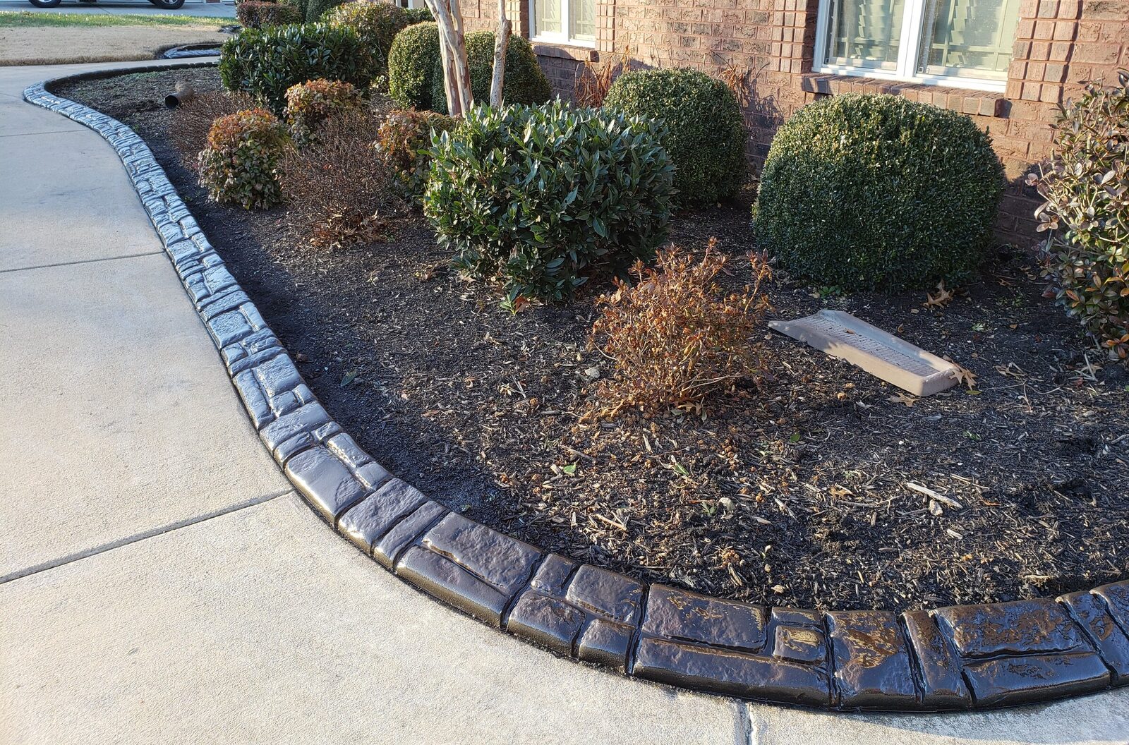 Dark stamped curbing along a driveway shrub bed